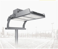 A large industrial outdoor stadium light fixture mounted on a pole, shown against a faded background of a sports court and fencing.