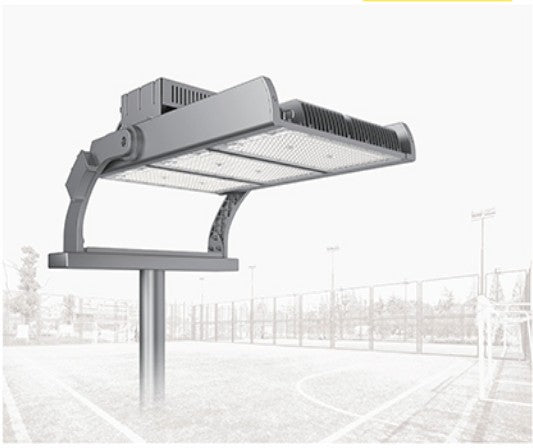 A large industrial outdoor stadium light fixture mounted on a pole, shown against a faded background of a sports court and fencing.
